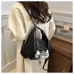 Detail der schwarzen Lederschultertasche mit süßem Plüschkatzen-Anhänger und Schleife