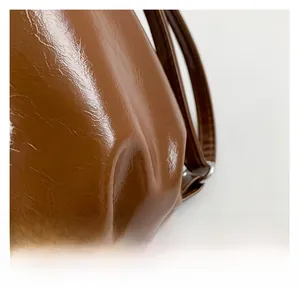 Close-up of brown glossy faux leather texture and metal strap buckle on tote bag