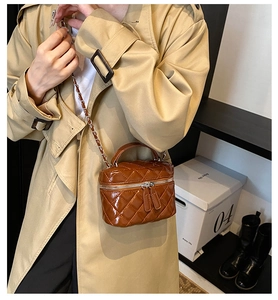 Detail of a brown quilted patent leather vanity bag with a gold chain strap and top handle