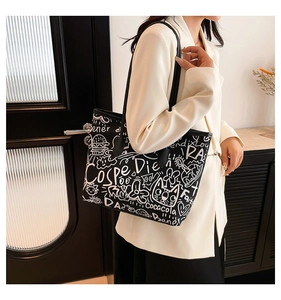 Detail of black tote bag with white graffiti patterns worn over a white blazer