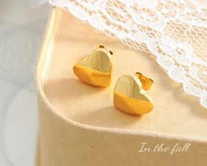 Detailed macro view of golden heart-shaped stud earrings with a polished mirror finish