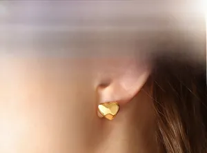 Close-up of model wearing gold heart stud earrings made of polished stainless steel