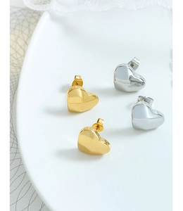 Polished gold and silver heart stud earrings set on a minimal white tray