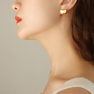 Elegant gold heart-shaped stud earrings in polished stainless steel on female model