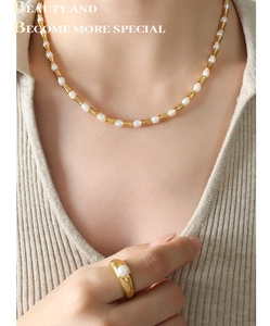 Dettaglio della collana in oro stile bambù e anello di perle su modella