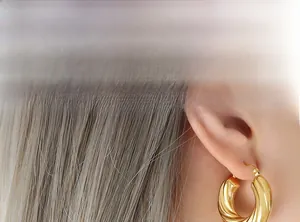 Vue macro de boucles d'oreilles créoles torsadées dorées portées par un mannequin