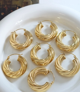 Détail de boucles d'oreilles créoles torsadées dorées avec texture en spirale sur assiette