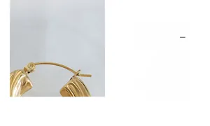 Détail de boucles d'oreilles en U dorées avec un design en métal torsadé texturé