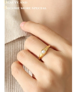 Dettaglio di un anello minimalista in titanio dorato con perla bianca tonda su scudo piatto