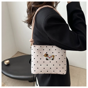 Détail du sac rose à pois avec broderie capybara porté sur un blazer noir élégant