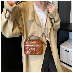 Detail of a brown patent leather quilted mini bag with chain strap on a model