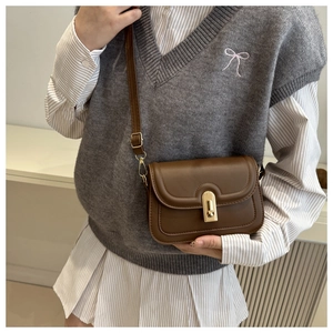 Gros plan du sac bandoulière vintage marron avec fermoir doré porté par le mannequin