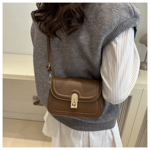 Petit sac bandoulière marron en cuir avec fermoir doré porté par un mannequin chic