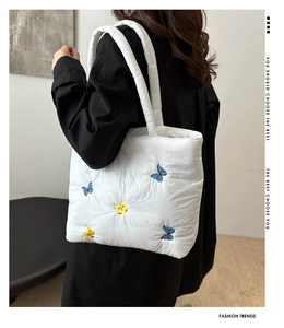 Detail of white quilted handbag featuring intricate butterfly embroidery and padded handle