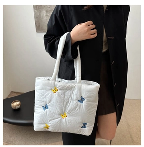 Detail of embroidered butterfly pattern on a white quilted shoulder tote bag