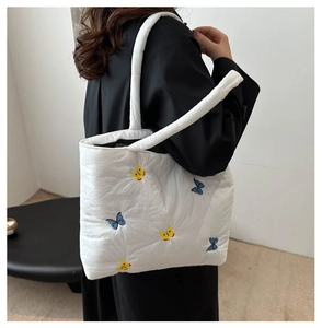Detailed embroidery of blue and yellow butterflies on a white quilted shoulder tote bag