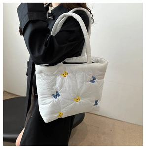Detail of white quilted tote bag featuring blue and yellow butterfly embroidery patterns