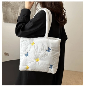 Detail of blue butterfly embroidery on a white quilted down tote bag with shoulder strap