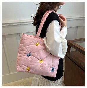 Pink quilted tote bag with butterfly embroidery worn over the shoulder by a model