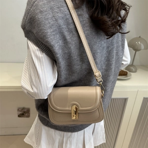 Sac bandoulière beige minimaliste avec fermoir doré porté par un mannequin en intérieur
