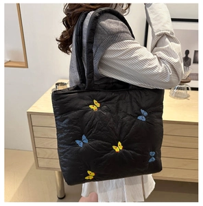 Detail of black quilted tote bag featuring vibrant butterfly embroidery and padded strap
