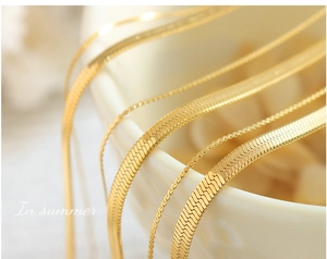 Detailed close-up of golden herringbone snake chains in various widths on white ceramic