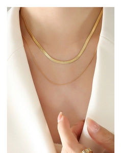 Detail of layered gold snake chain and thin link necklace on a model wearing a white suit