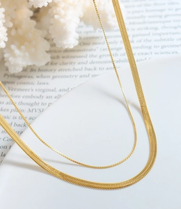 Detail of layered gold snake chain and beaded necklace set with a polished metallic finish