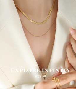 Close-up of layered gold snake chain necklace and safety pin ring on female model