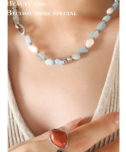 Détail d'un collier de perles bleues et nacre avec une bague rétro en pierre rouge vif