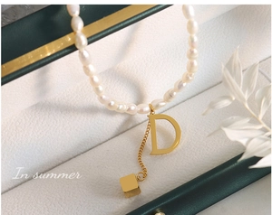 Macro shot of freshwater pearl necklace with gold letter D pendant and cubic charm