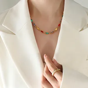Golden necklace with rainbow rectangular gemstones worn by a model in a white blazer