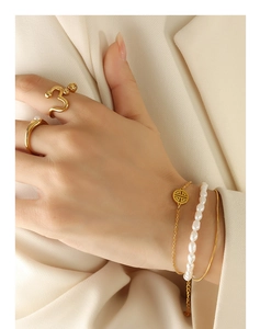Detail of layered gold rings and pearl bracelet with hollow pendant on model
