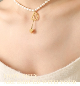 Detailed close-up of a pearl necklace with golden D-letter and square cube charms