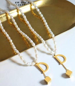 Macro detail of freshwater pearl necklace with gold letter D and cube tassel pendant