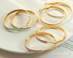 Close-up of three pairs of textured gold hoops with mint, lilac, and white enamel details