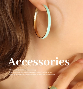 Close-up of gold hoop earrings with mint green enamel inlay worn by a model