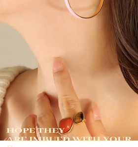 Detailed shot of large golden hoop earrings with pink enamel inlay and double stone rings