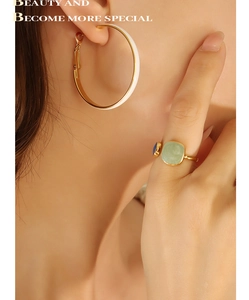 Close-up of golden enamel hoop earrings and square gemstone ring worn by a model