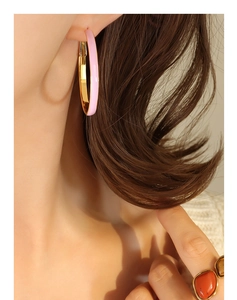 Close-up of model wearing chunky pink enamel and gold hoop earrings with retro flair
