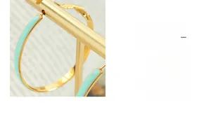 Detail of C-shaped gold metal earrings with mint green enamel on a golden display stand