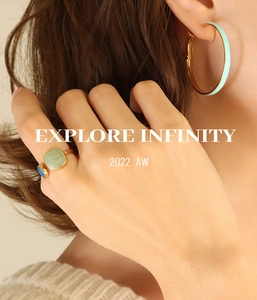 Close-up of model wearing gold open ring and large hoop earrings with light green enamel