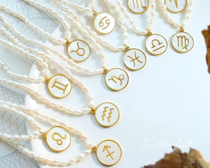 Detailed close-up of zodiac pearl necklaces with gold-rimmed white shell pendants in a fan layout