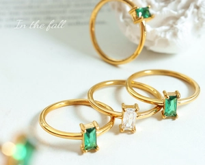 Detail of four gold rings with rectangular green and white cubic zirconia stones