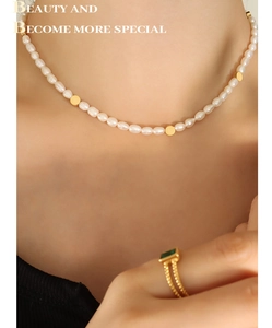 Close-up of freshwater pearl necklace with gold beads and a green gemstone ring