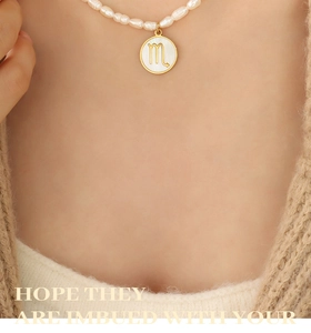 Close-up of Scorpio zodiac pearl necklace with gold circular shell pendant and knitwear