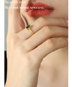 Close-up of minimalist gold ring with emerald-cut green zircon on a model finger