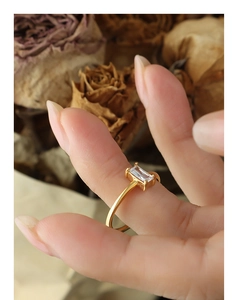 Macro detail of a golden ring with a rectangular cubic zirconia on a warm floral background