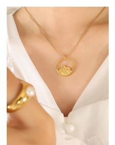 Detail of gold mountain relief pendant necklace and pearl ring on a model in white shirt
