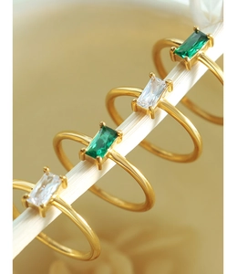 Macro detail of four gold minimalist rings with square-cut emerald and white zircon stones
